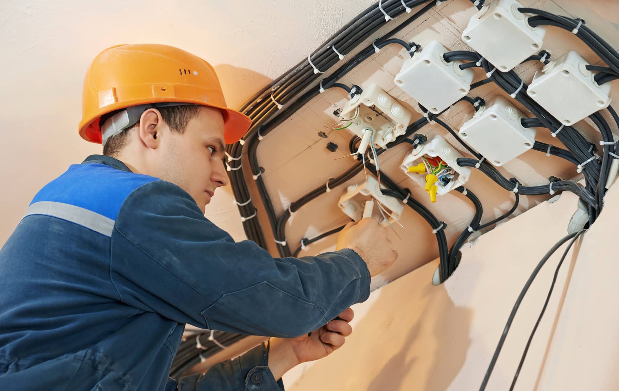 Mann mit orangenem Helm arbeitet an einer Verkabelung